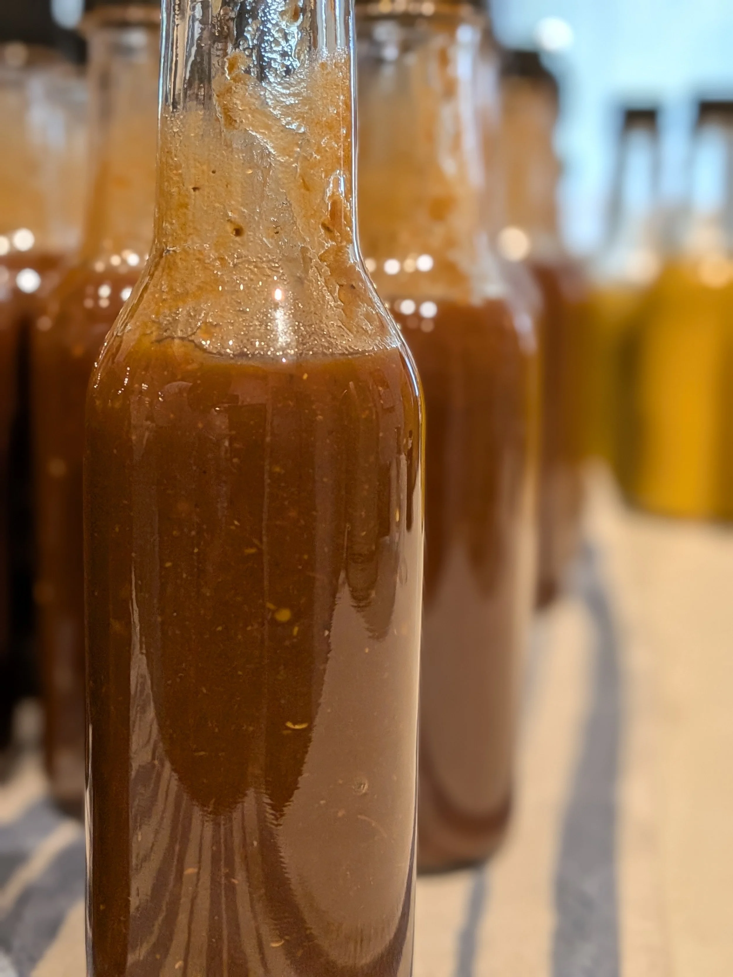Close-up of a row of glass bottles filled with dark brown liquid, likely syrup or sauce, with condensation forming on the outside of the bottles.
