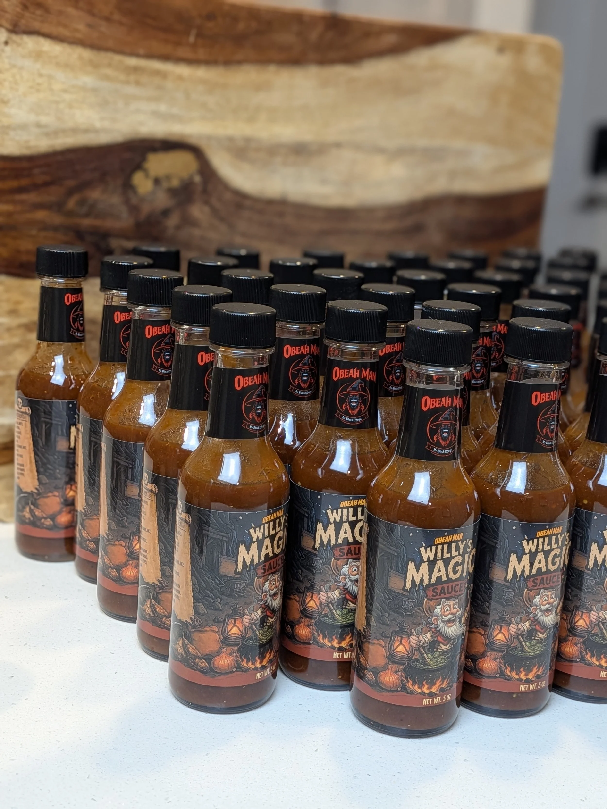Multiple bottles of Willy's Magic Sauce with a prospector and fantasy design on the label, arranged on a white surface.