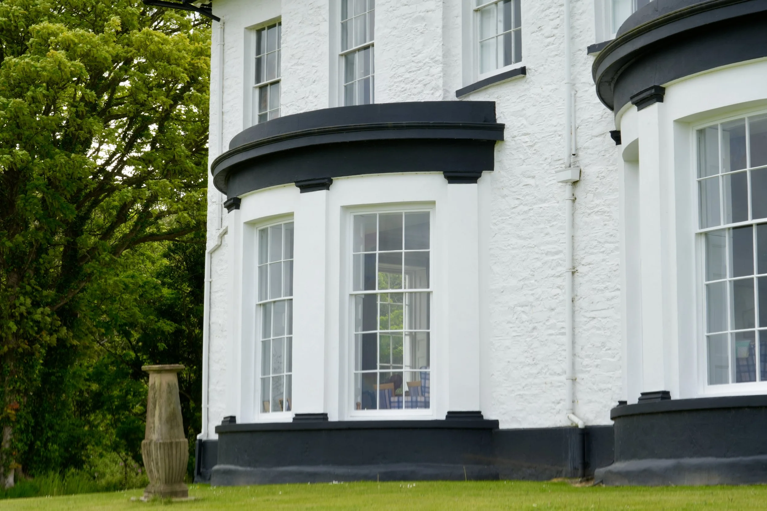 White house exterior with large windows and black accents, surrounded by green trees and a grass lawn.