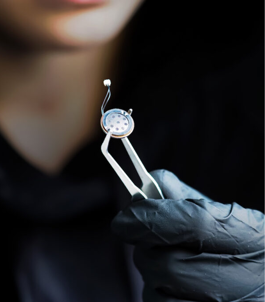 Close-up of a person's gloved hand holding a small metallic dental tool with a circular component, used in dental implant procedures.