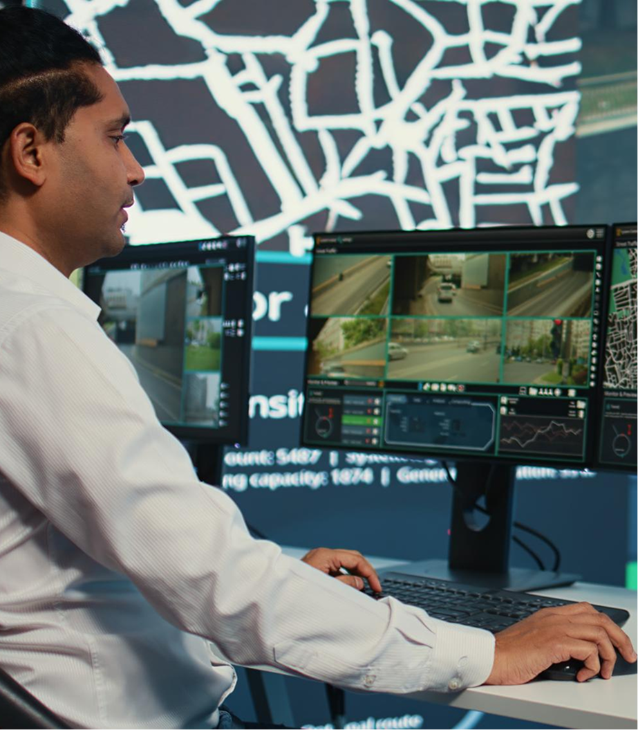A man working at a desk with multiple monitors showing surveillance footage of traffic cameras