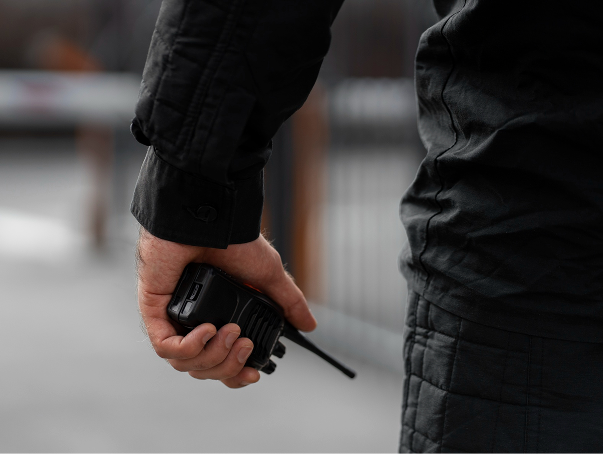 A person dressed in black holding a walkie-talkie in their right hand.