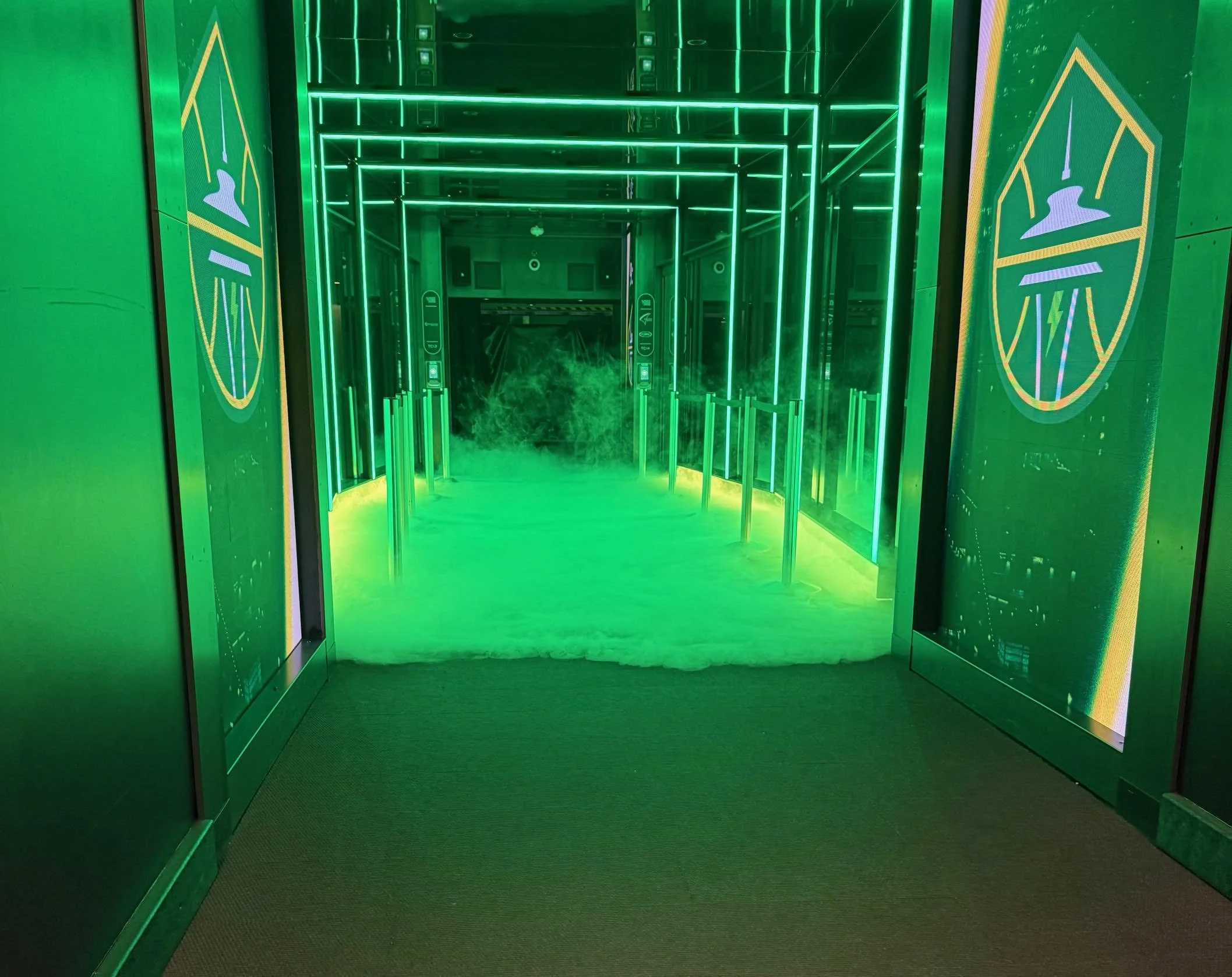 Green lit corridor with mirrored walls and ceiling, and signs displaying a white hand with a red line and an arrow on a green background.