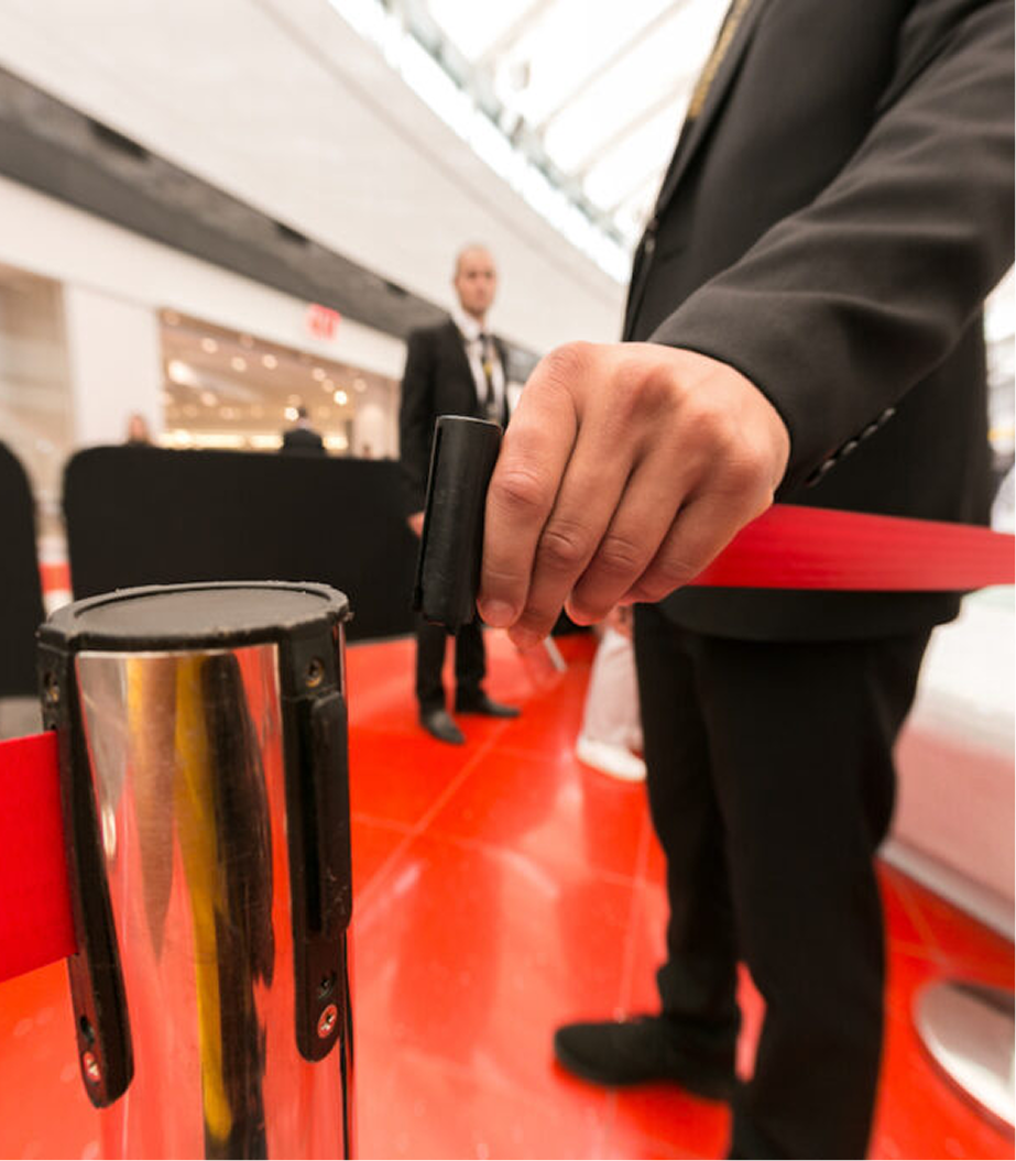 A person in a suit using a handheld tool to set up a red barrier at an indoor event space.
