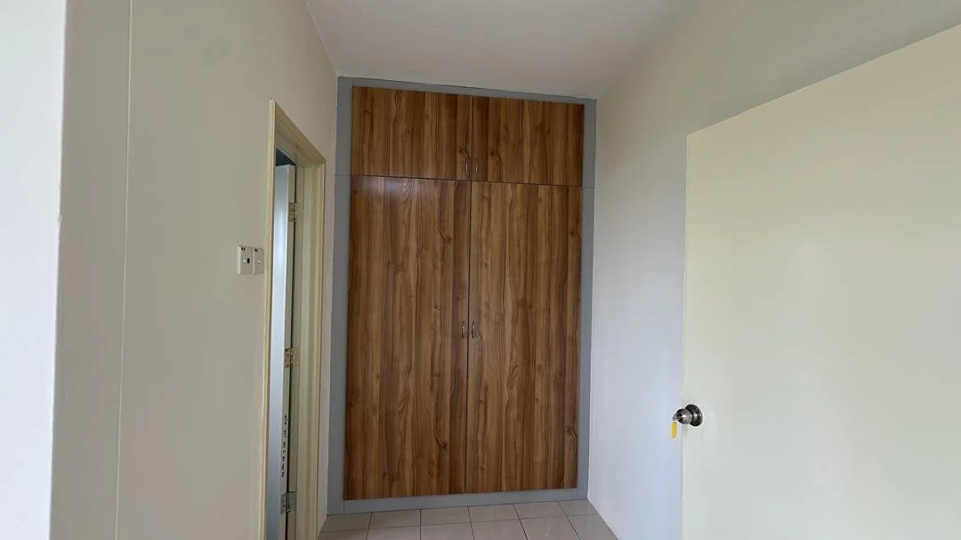 Interior view of a room showing a wooden built-in closet with two doors, beige walls, a door on the left, and a tiled floor.