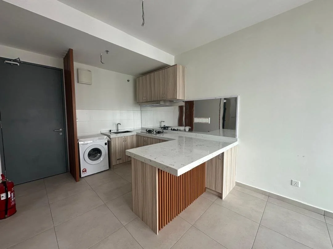Empty modern kitchen with light wood cabinets, a white patterned countertop, a washing machine, stove, and sink. Grey door on the left, fire extinguishers set nearby, and a small window opening to the living area.