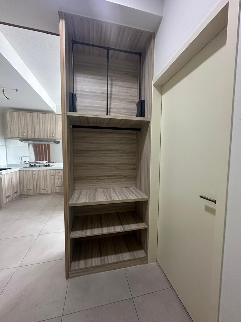 Empty wooden shelving unit with four shelves, located next to a beige door in a kitchen area with tiled floor.