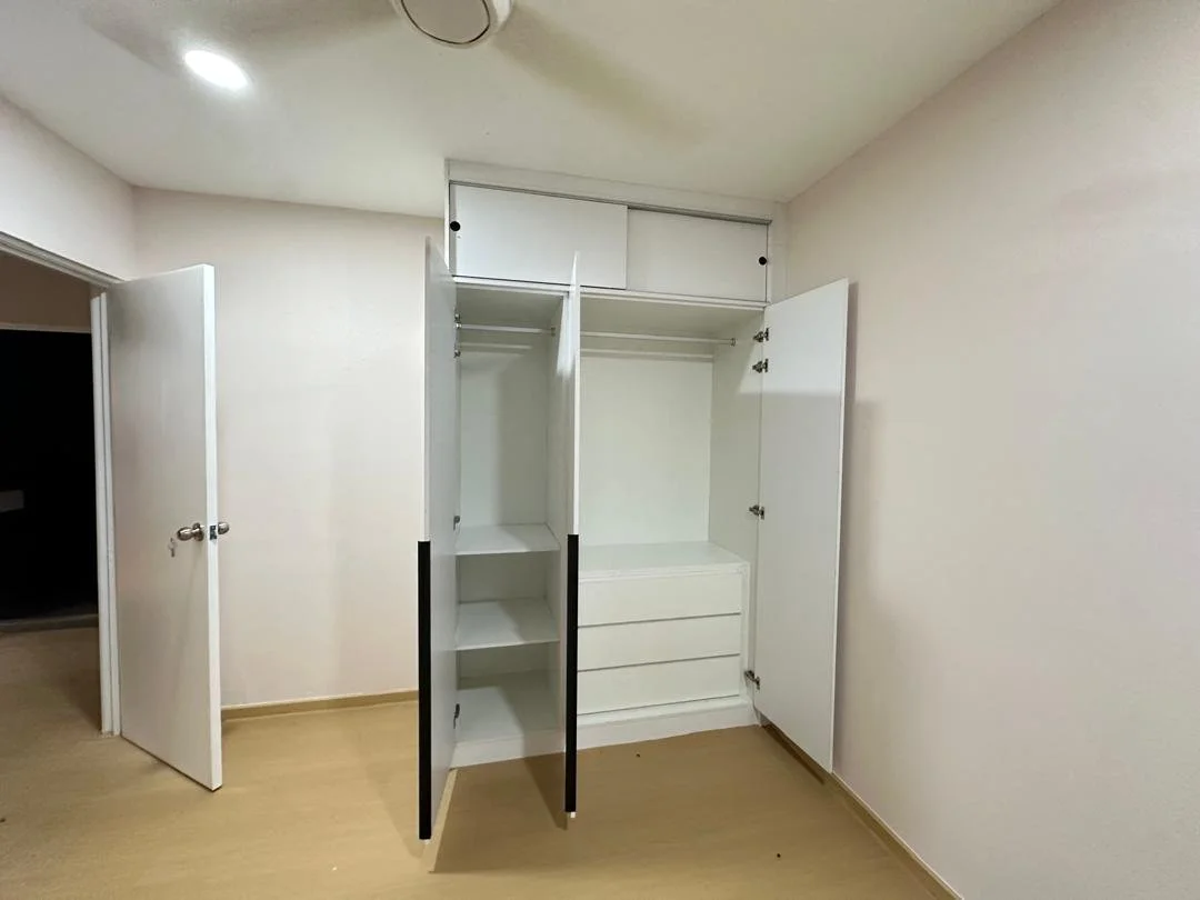 Empty built-in closet with open doors, shelves, and drawers in a room with beige walls and light wooden flooring.