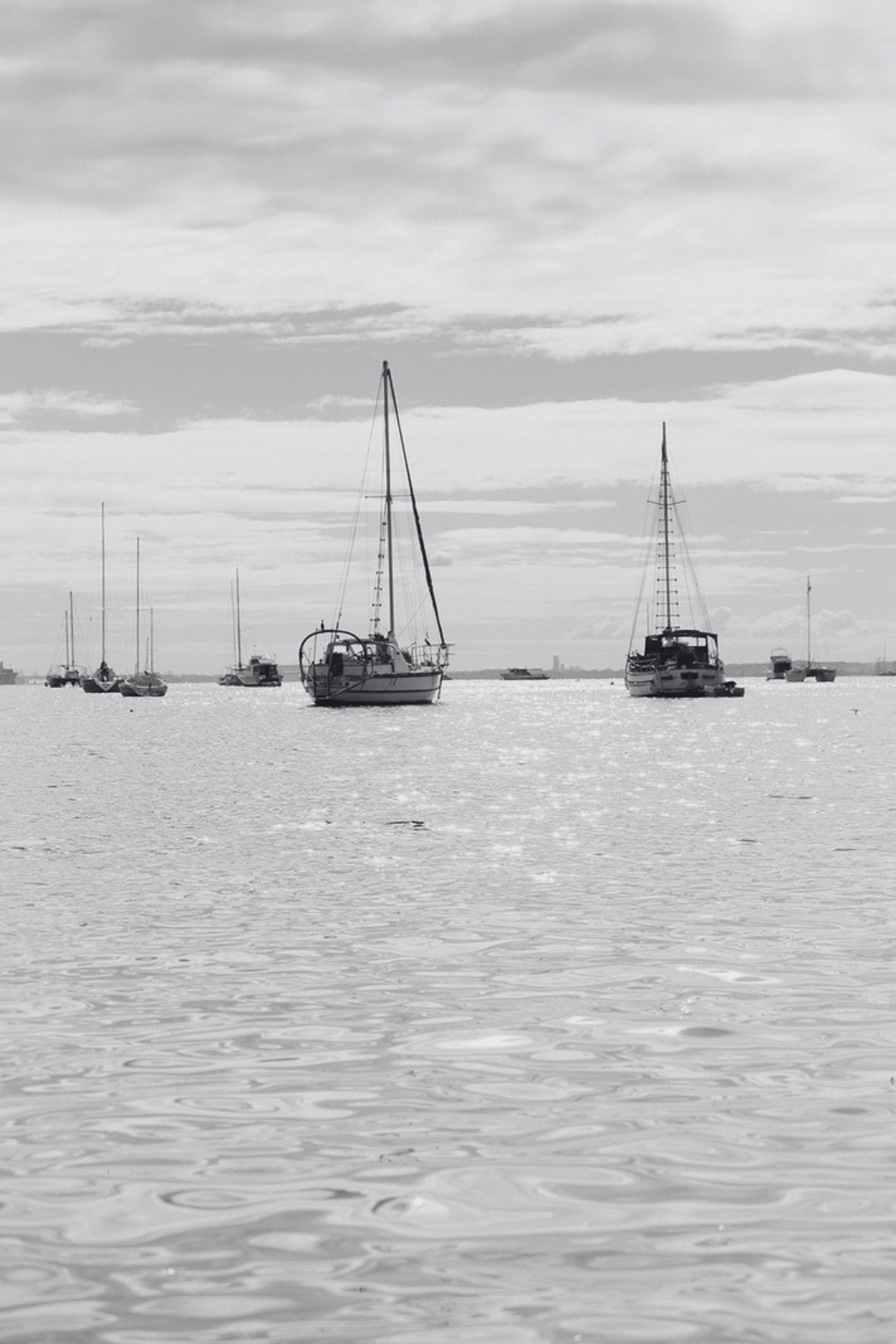 Several sailboats and yachts floating on calm water under a cloudy sky.