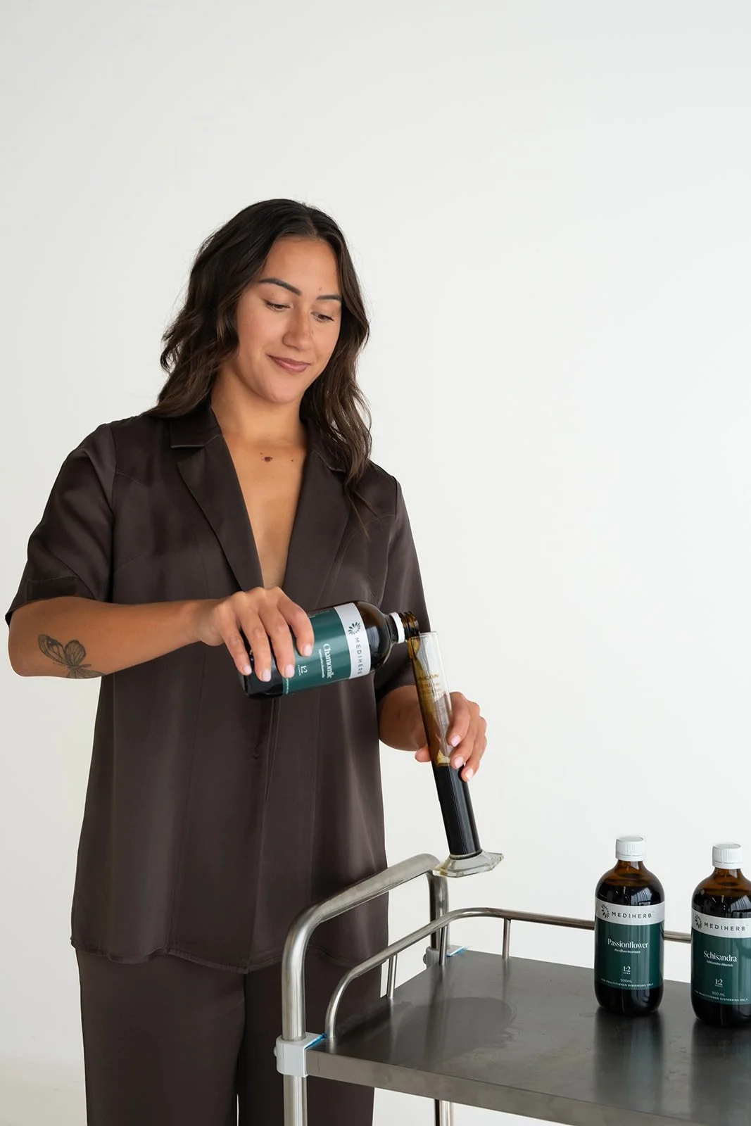 Woman pouring liquid from a dark green bottle into a test tube on a medical cart.
