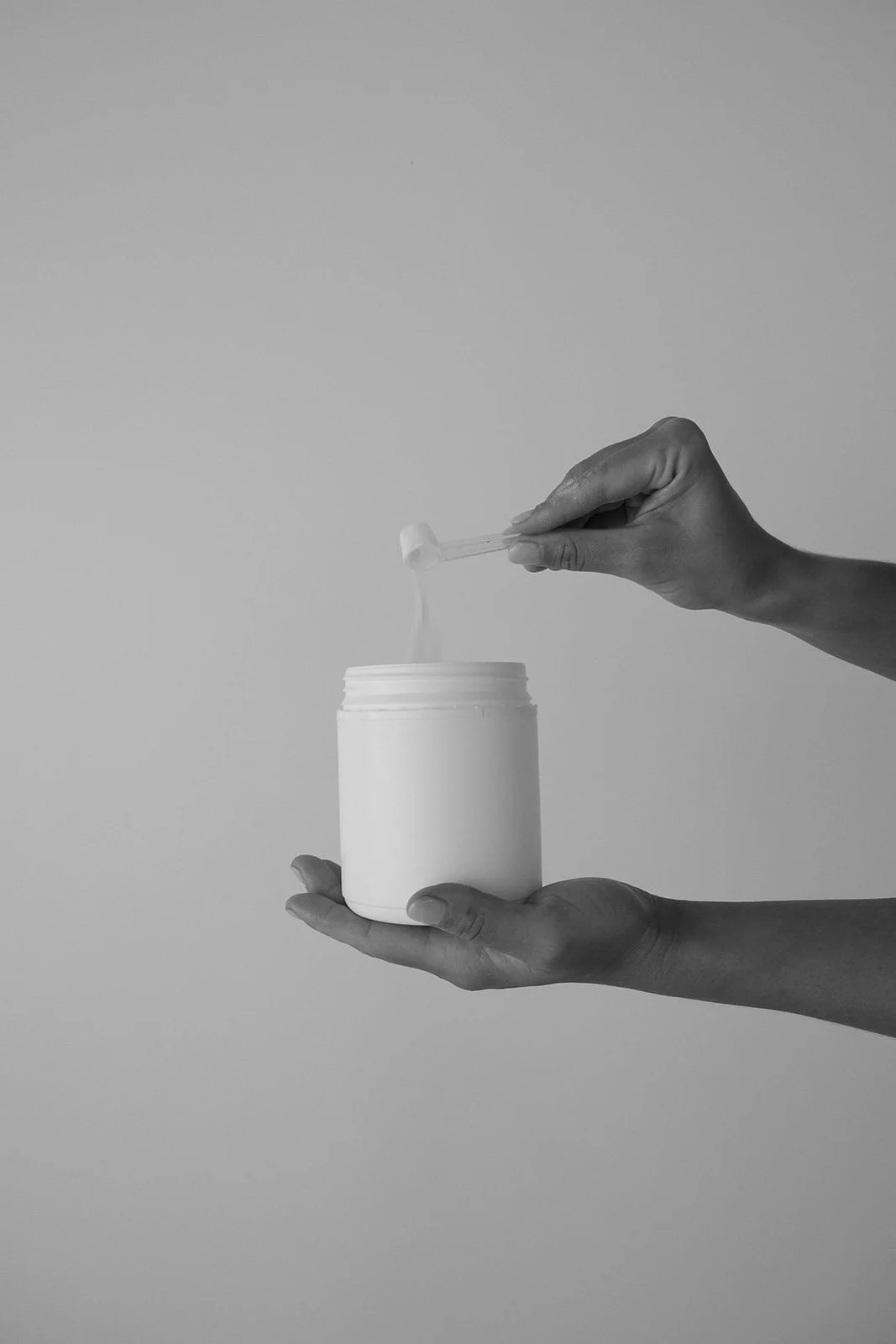 A person's hand holding a container while another hand is pouring powder into it, against a plain background.