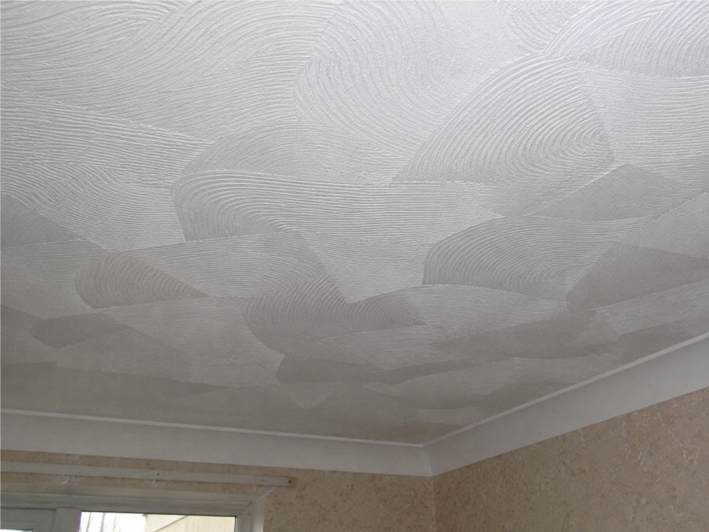 Decorative textured ceiling with abstract swirling patterns in a room with beige walls and a window.