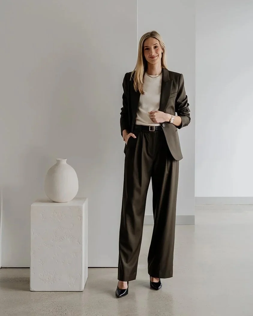 Rebecc Simmons standing in foyer of Simmons Legal office in melbourne cbd. She has long blonde hair and is smiling, with her hands in her pockets. There is a white vase on a pedestal to her left.