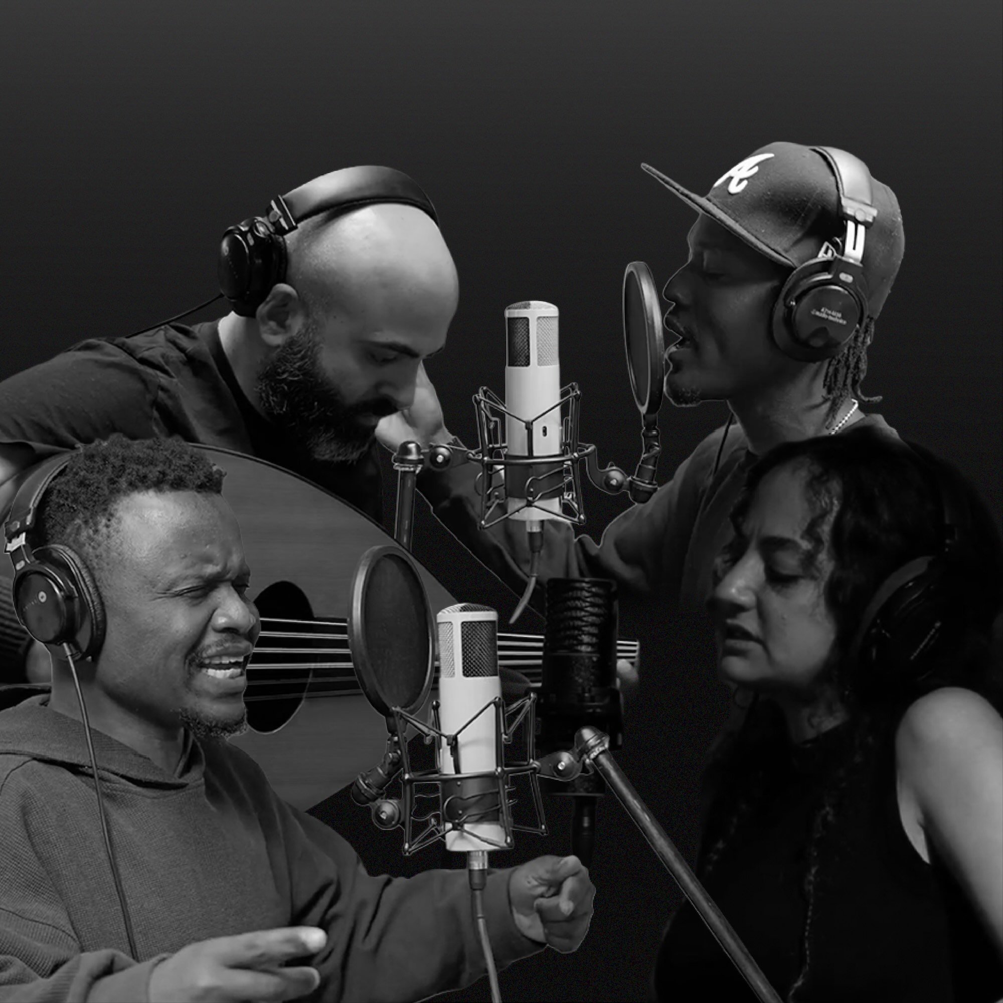 Four musicians singing into microphones in a recording studio with headphones on. They are almost facing each other, immersed in singing.