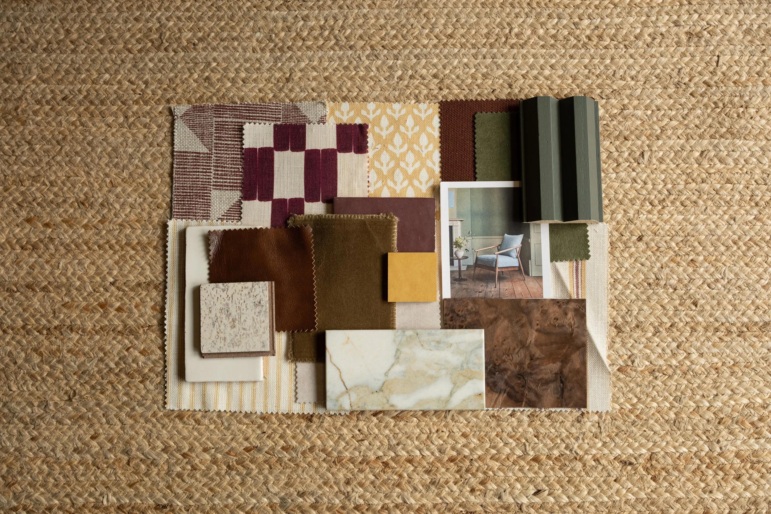 A collection of fabric swatches, tiles, and a photo of a room interior sample arranged on a woven surface.