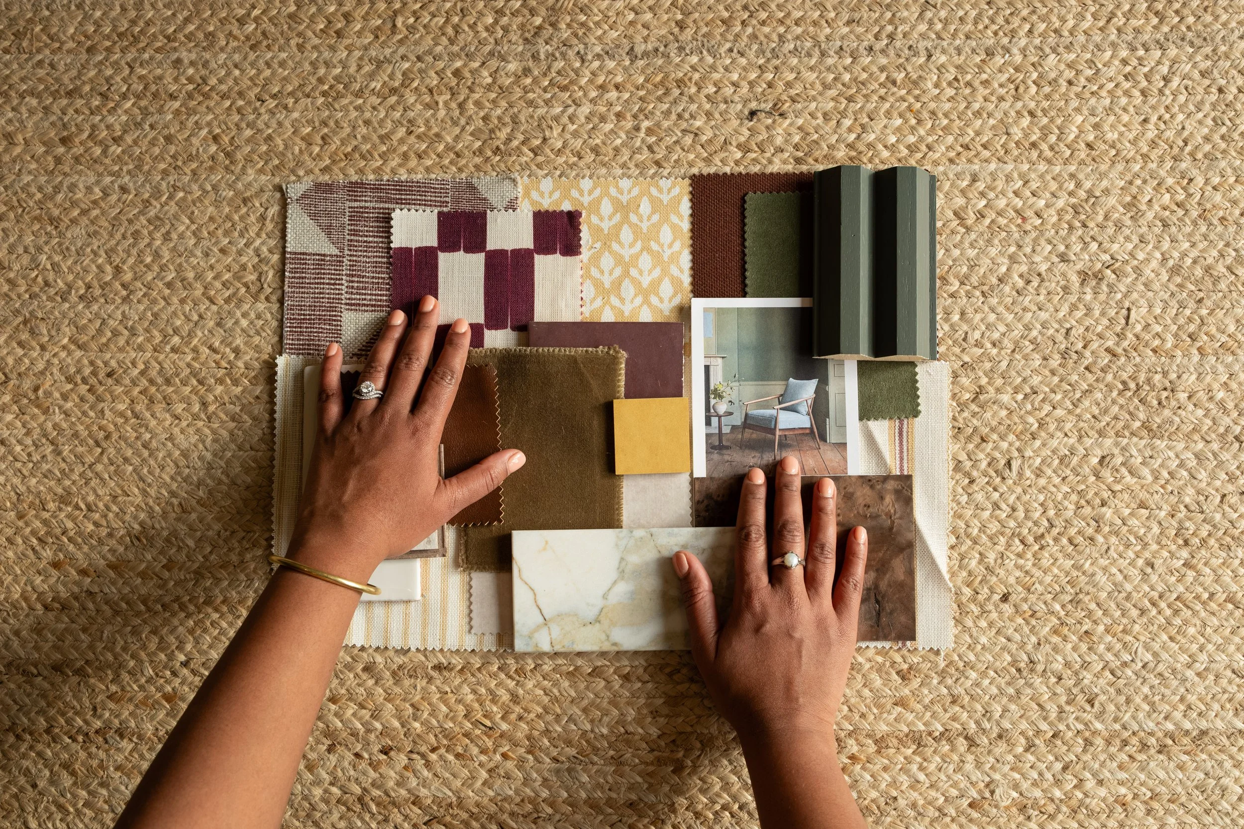 A person arranging fabric swatches for interior design on a woven surface.