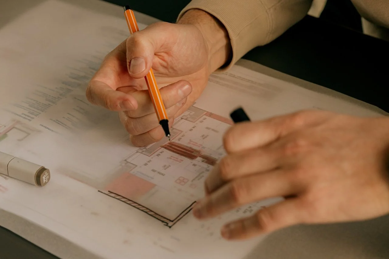 Hands working on an architectural floor plan with markers and a pen.