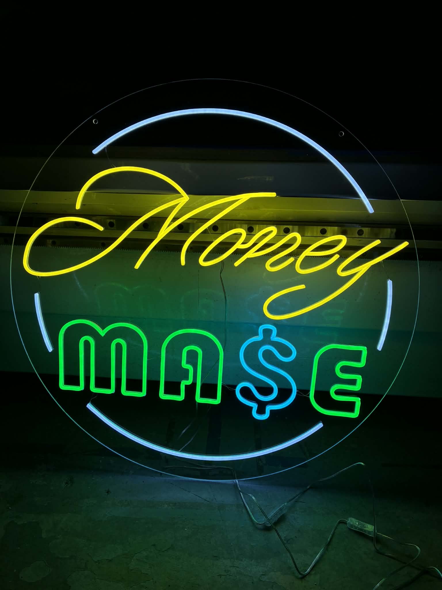 A neon sign with the words 'Money' in yellow cursive at the top and '$' and '¢' symbols in blue and green at the bottom. The sign is illuminated in a dark setting.
