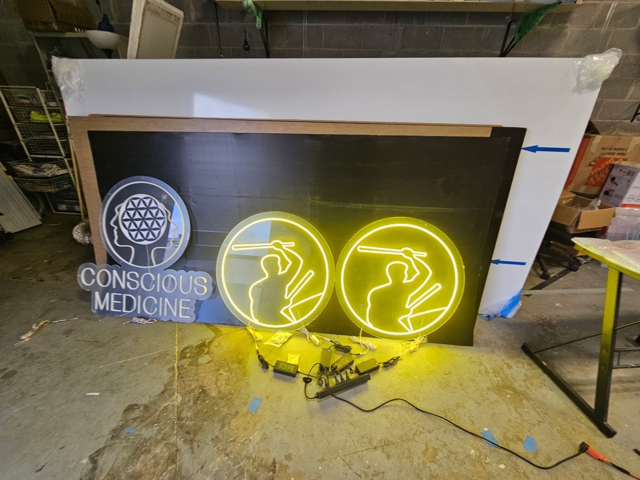 Neon sign of a woman doing yoga with the words 'Conscious Medicine' underneath, placed on a floor in a workshop.