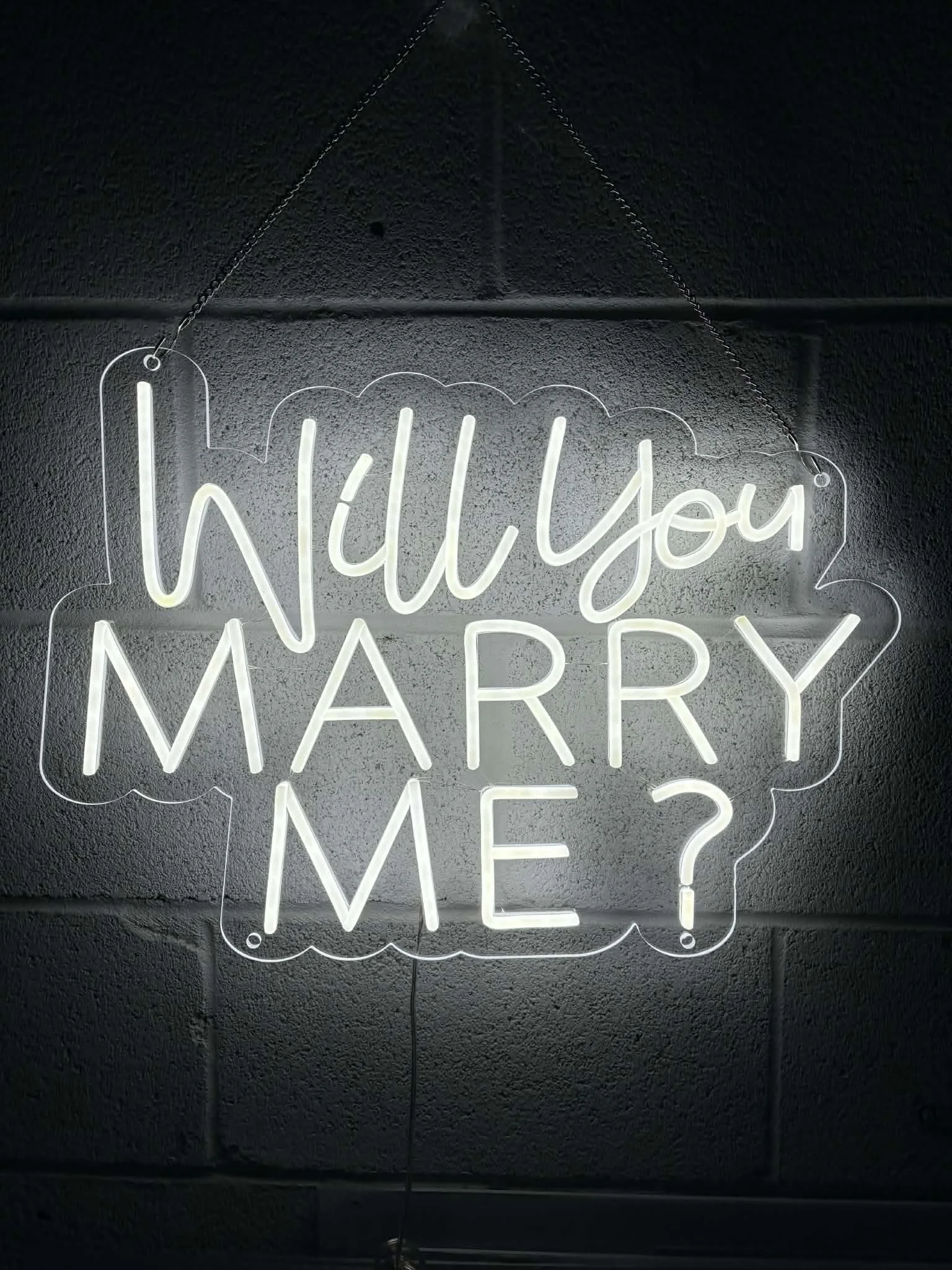 Neon sign on a dark wall reading 'Will you marry me?' in cursive style.