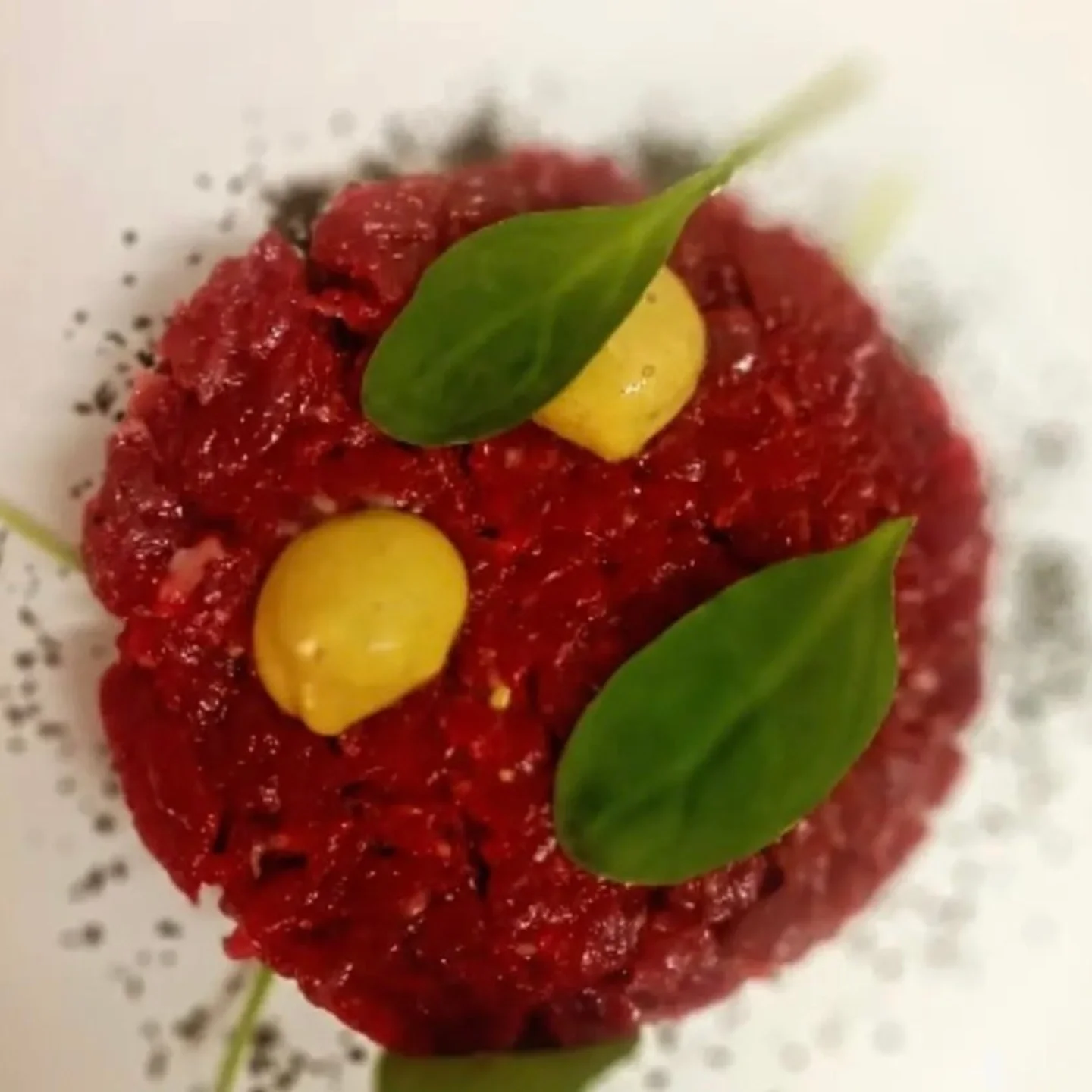 Tartare di carne rossa decorato con foglie verdi e capperi