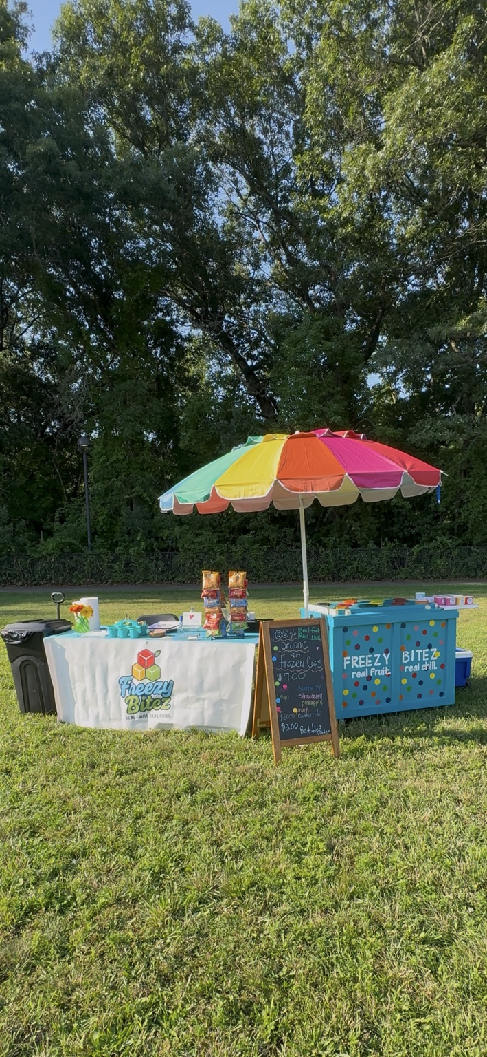 Freezy Bitez turquoise cart under a colorful umbrella at a community event