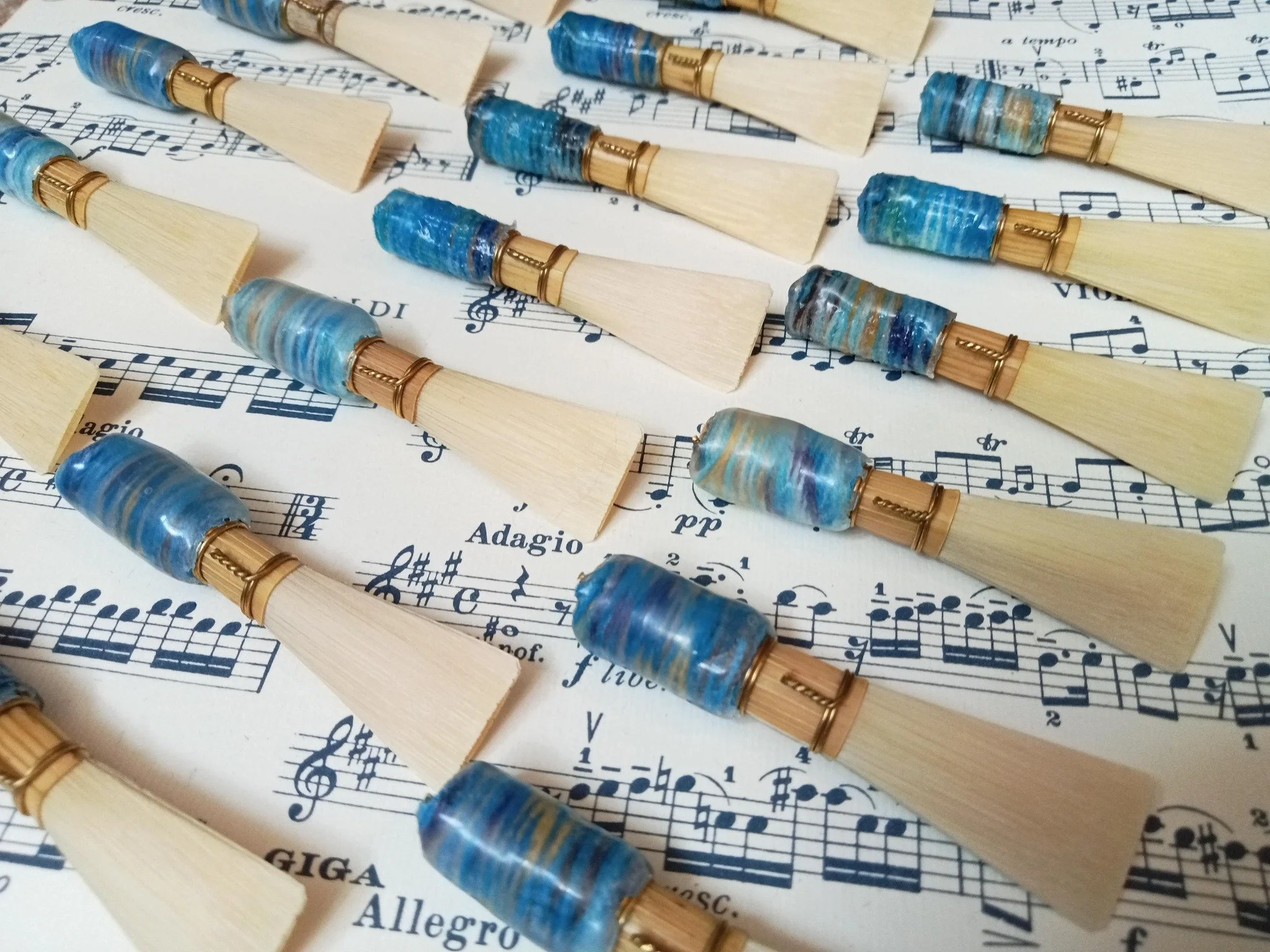 Close-up of several bassoon reeds in colourful London Reeds standard blue thread, laid on sheet music with musical notations and words like "Adagio" and "Allegro."