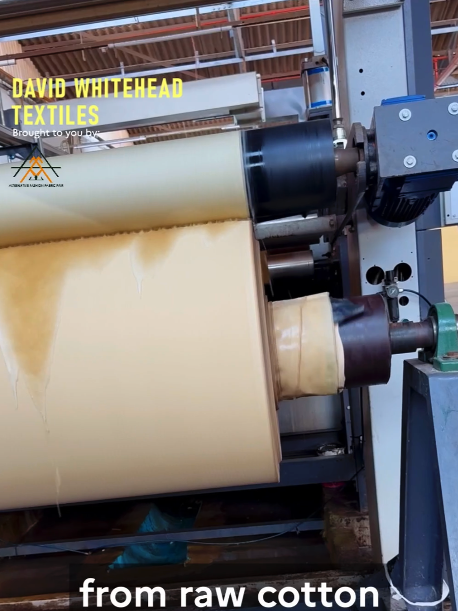 Close-up of a machine processing raw cotton into textile material in a factory setting, with visible rollers and industrial equipment.