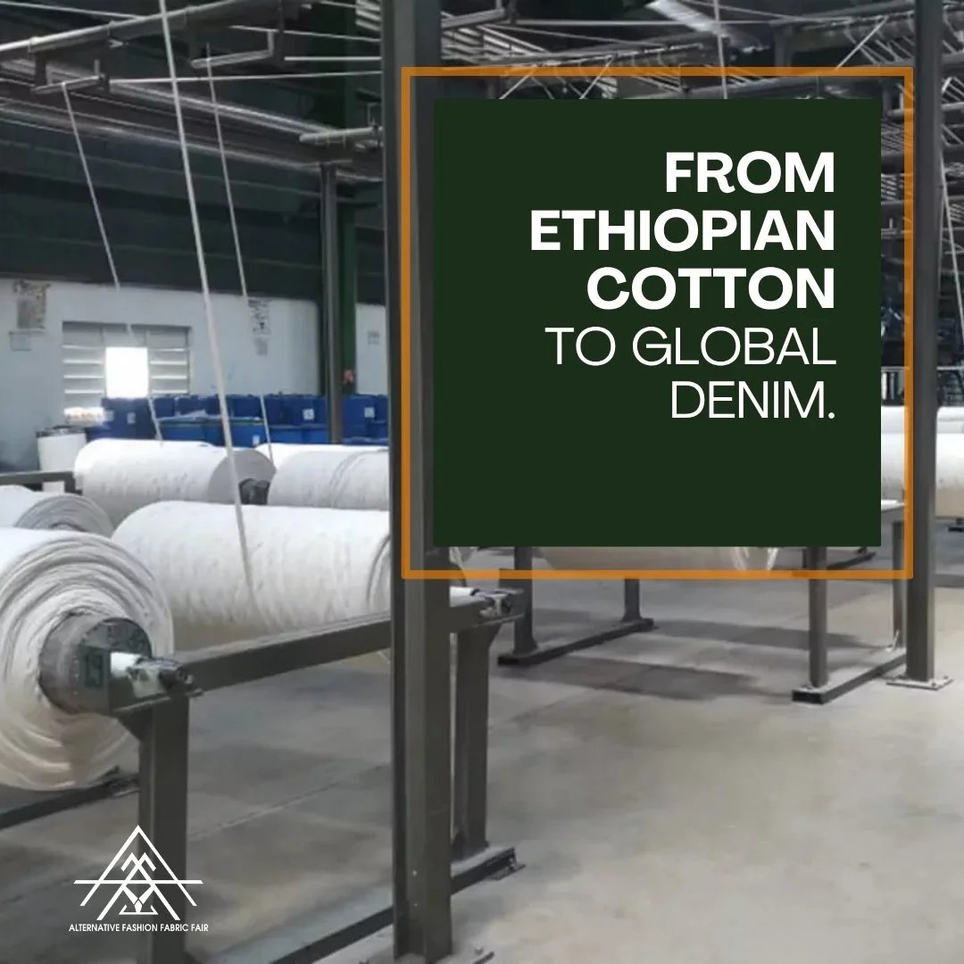 Text on a sign in a textile factory reads 'From Ethiopian Cotton to Global Denim.' The background shows rolls of white fabric and industrial machinery.