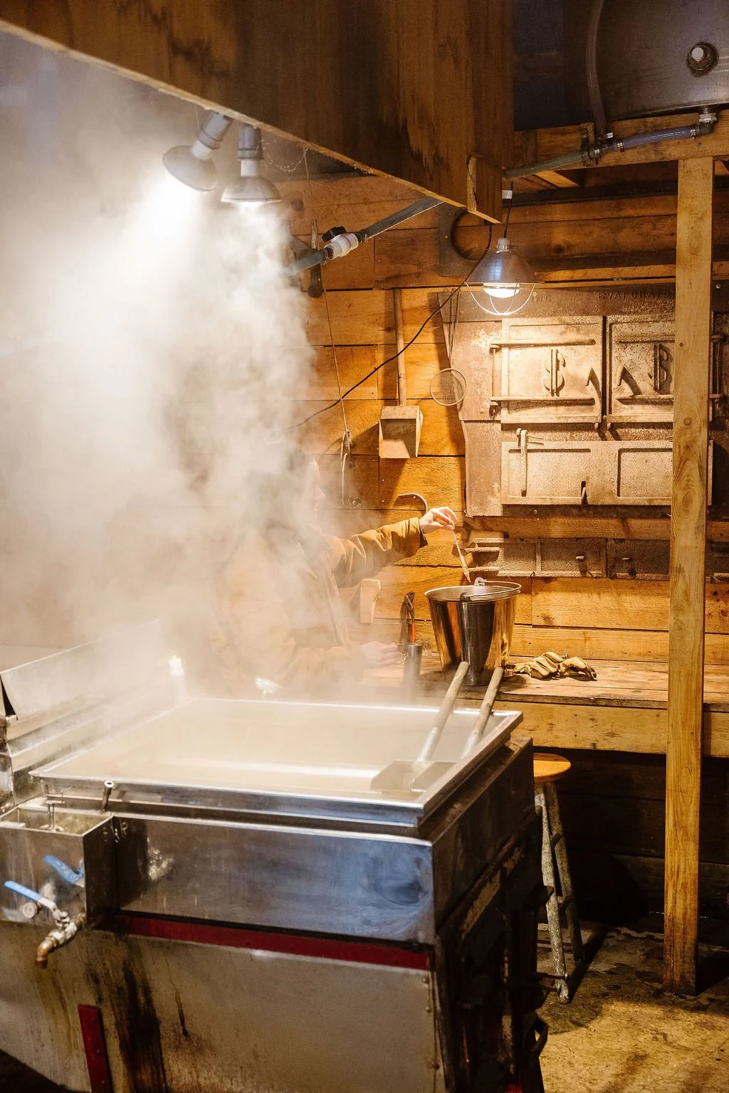 A person is seen in a rustic wooden kitchen, preparing food with steam rising from a large metal pot on an old stove. The scene has warm lighting and a cozy, vintage feel.