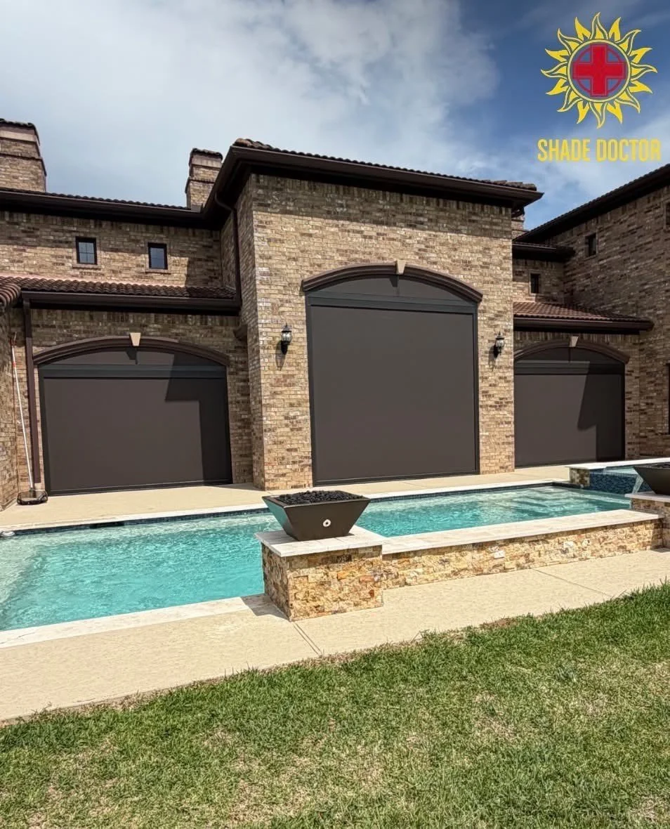 A house with a brick exterior featuring three large dark-colored garage doors, a swimming pool in the backyard, and outdoor lighting. The sky is partly cloudy, and a logo with a sun and cross, along with the text 'Shade Doctor,' is in the top right corner.
