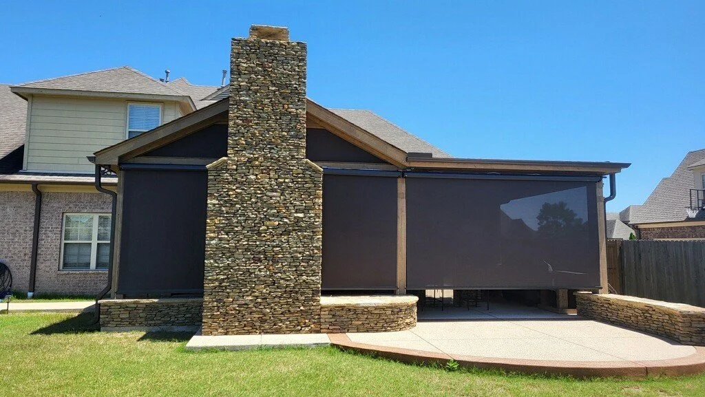 Backyard with a stone chimney, screened porch and a concrete patio with rounded edge.
