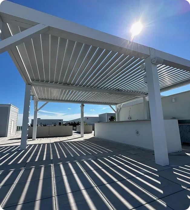 Modern rooftop terrace with white pergola casting striped shadows, clear blue sky, and bright sunlight.