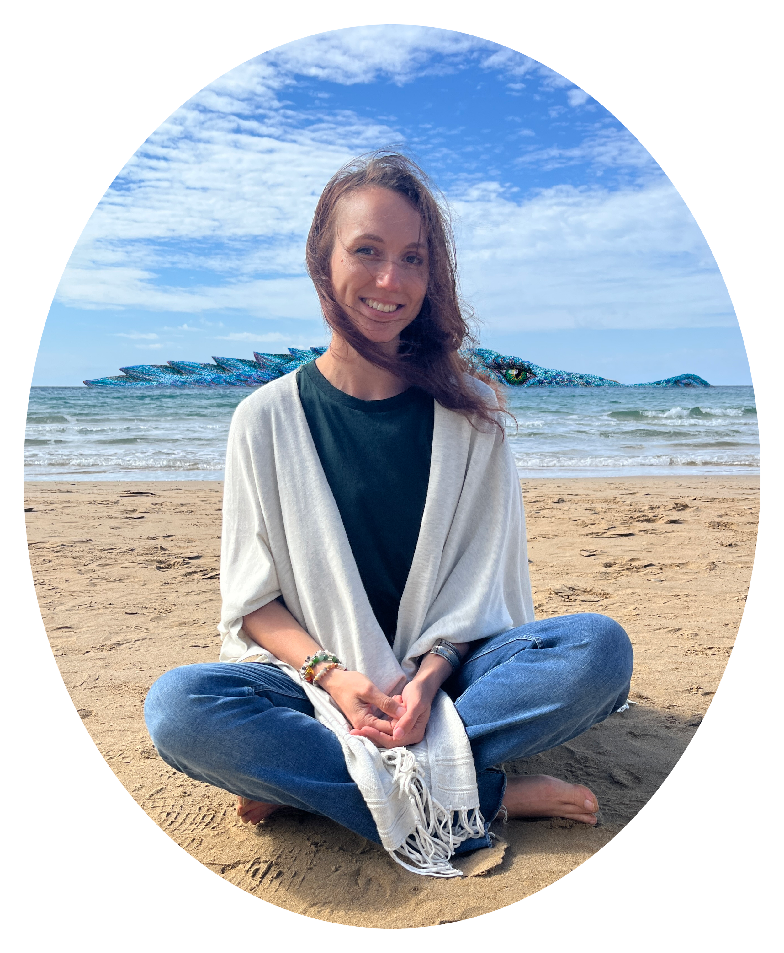 A woman with long brown hair sitting cross-legged on a sandy beach with a blue sky and clouds in the background. She is smiling, wearing a gray cardigan over a black shirt, and has bracelets on her wrist. Behind her, a dragon peeks out of the sea.