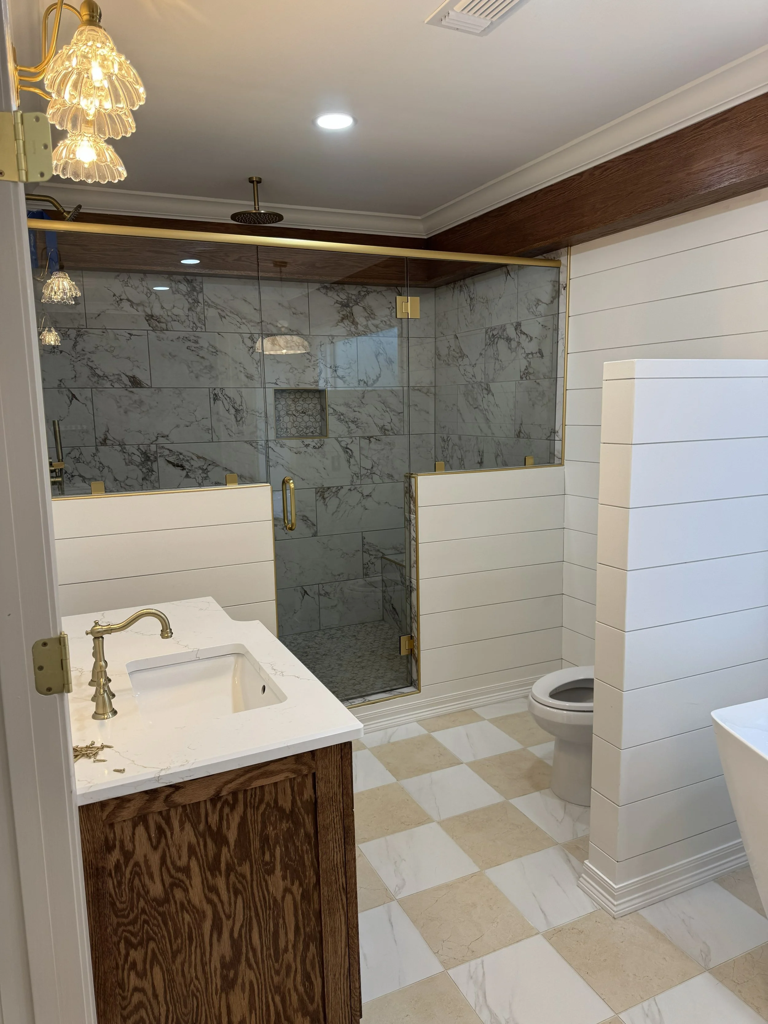 A bathroom with a marble tiled shower, a white toilet, a wooden vanity with a white sink, and decorative lighting fixtures.