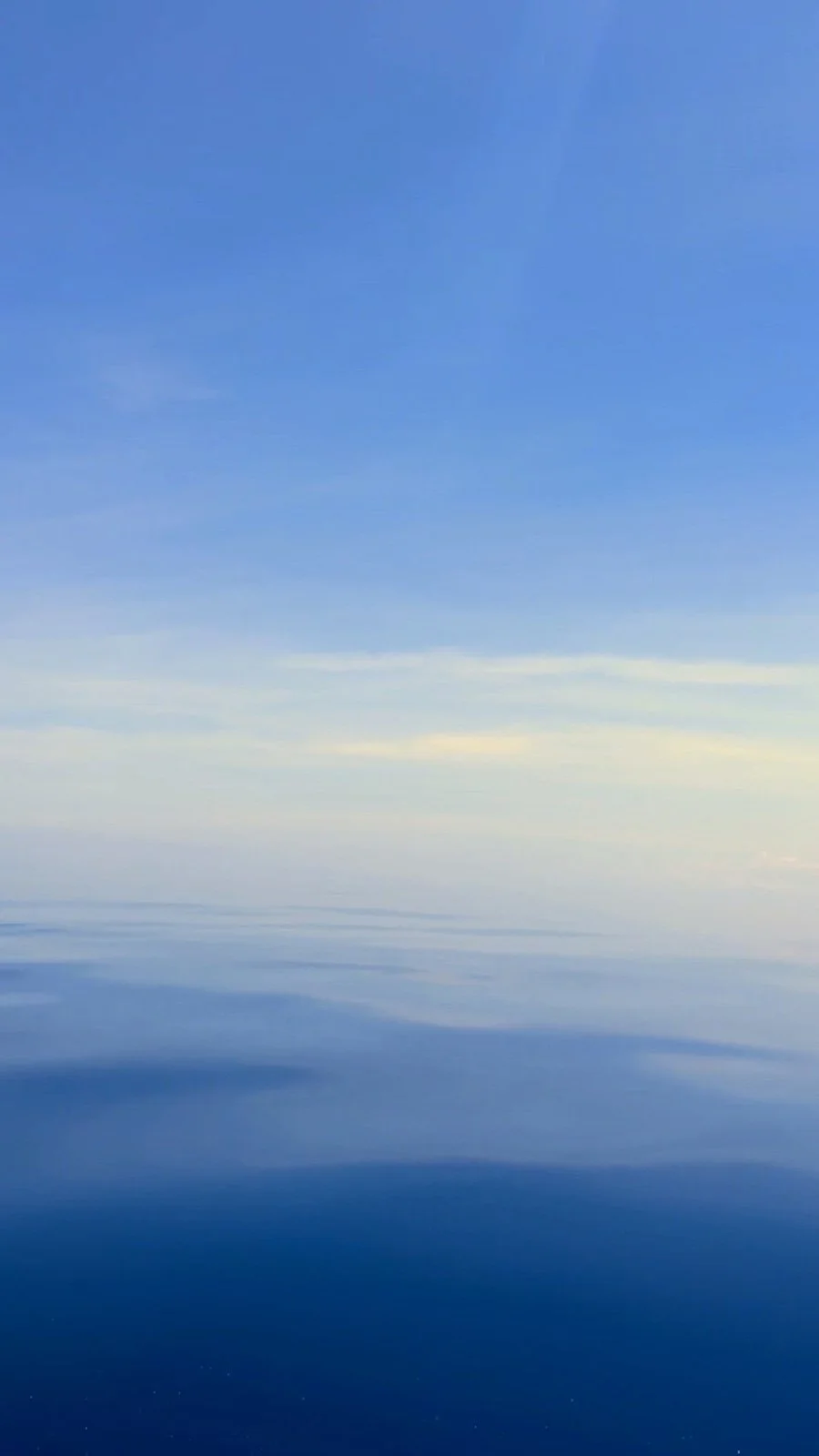 Sky and water reflecting each other, with blue and light yellow hues and a few wispy clouds
