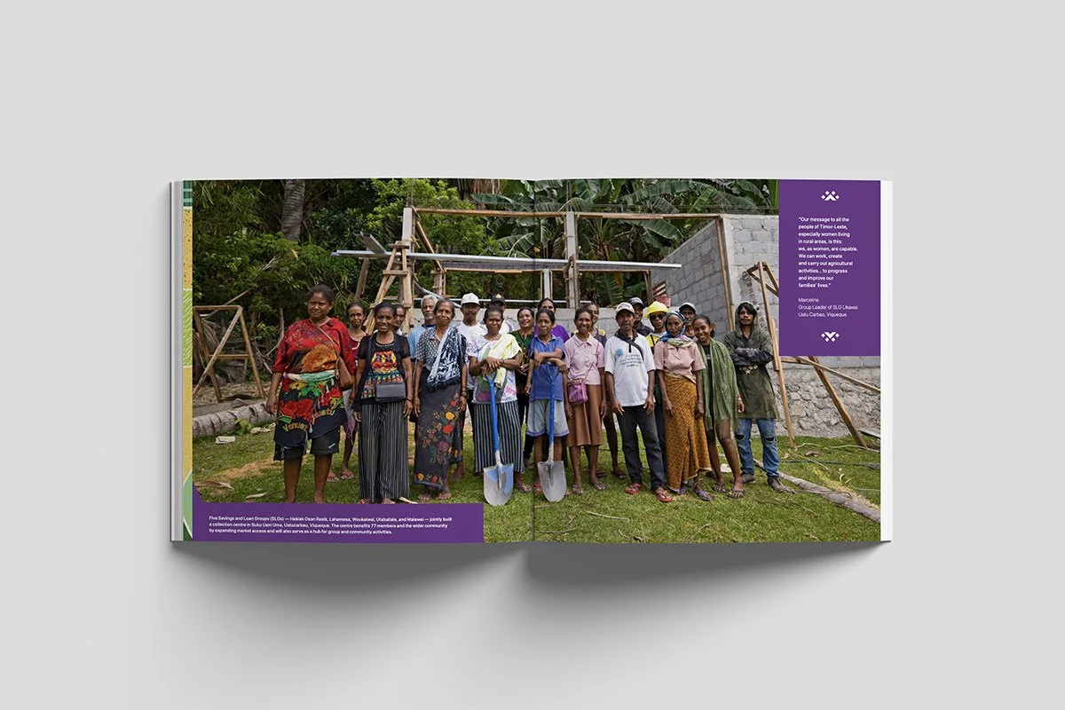 Group of people standing outdoors on a grassy area in front of a partly constructed building, some holding shovels, with trees and vegetation in the background.