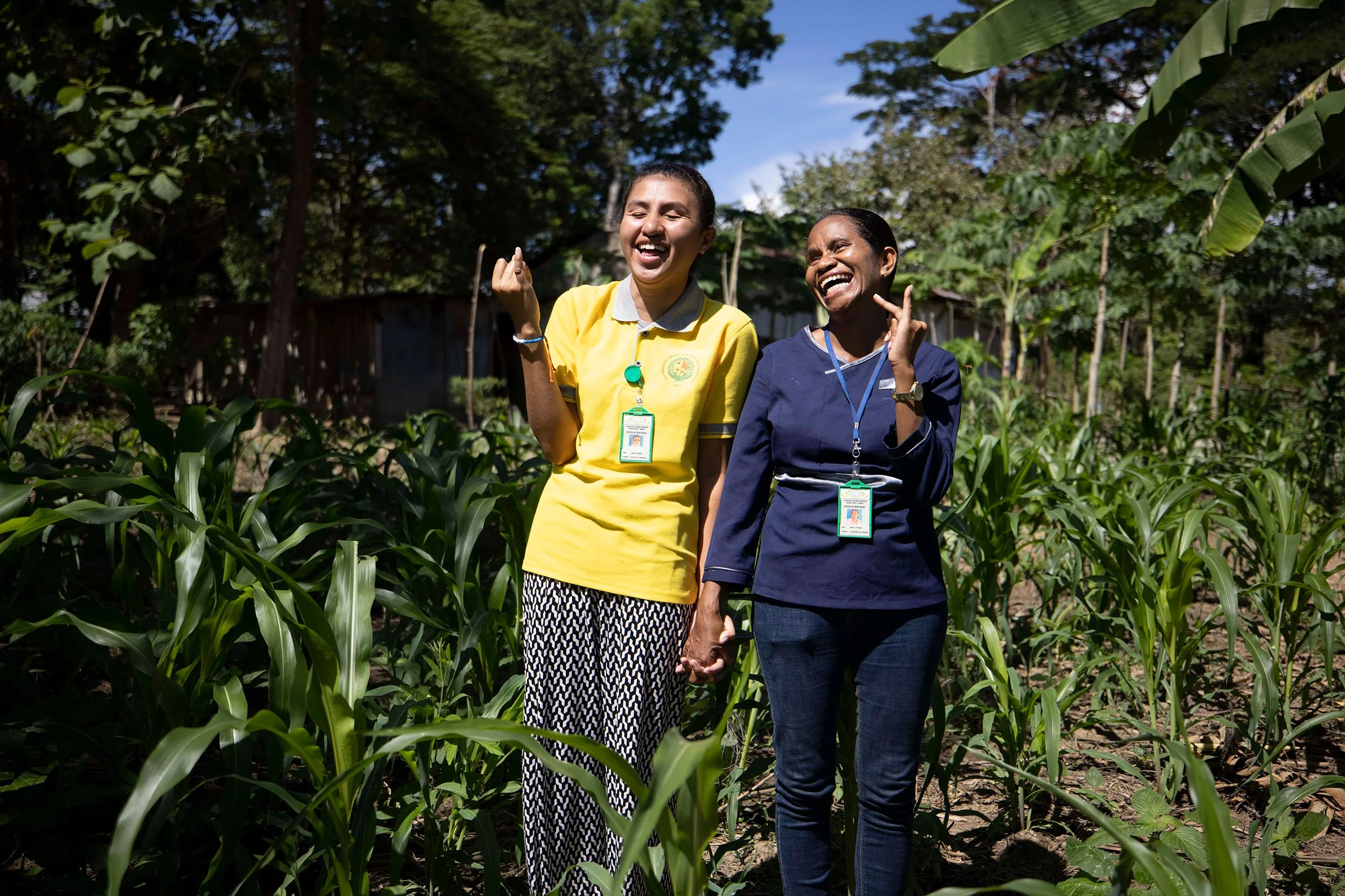 Two women standing in a lush green garden, holding hands and smiling joyfully.