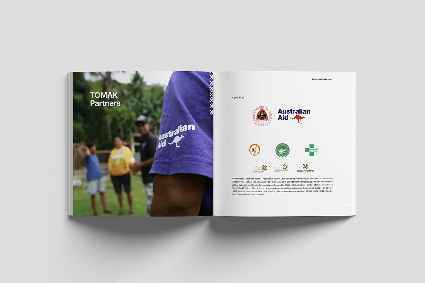 Open magazine featuring a photo of people outdoors, with the focus on a person wearing a purple shirt with the Australian Aid logo, and the text 'TOMAK Partners'. The right page displays several logos, including Australian Aid and others.