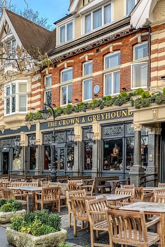 Exterior of a pub called 'The Crown & Greyhound' with outdoor seating and wooden chairs and tables