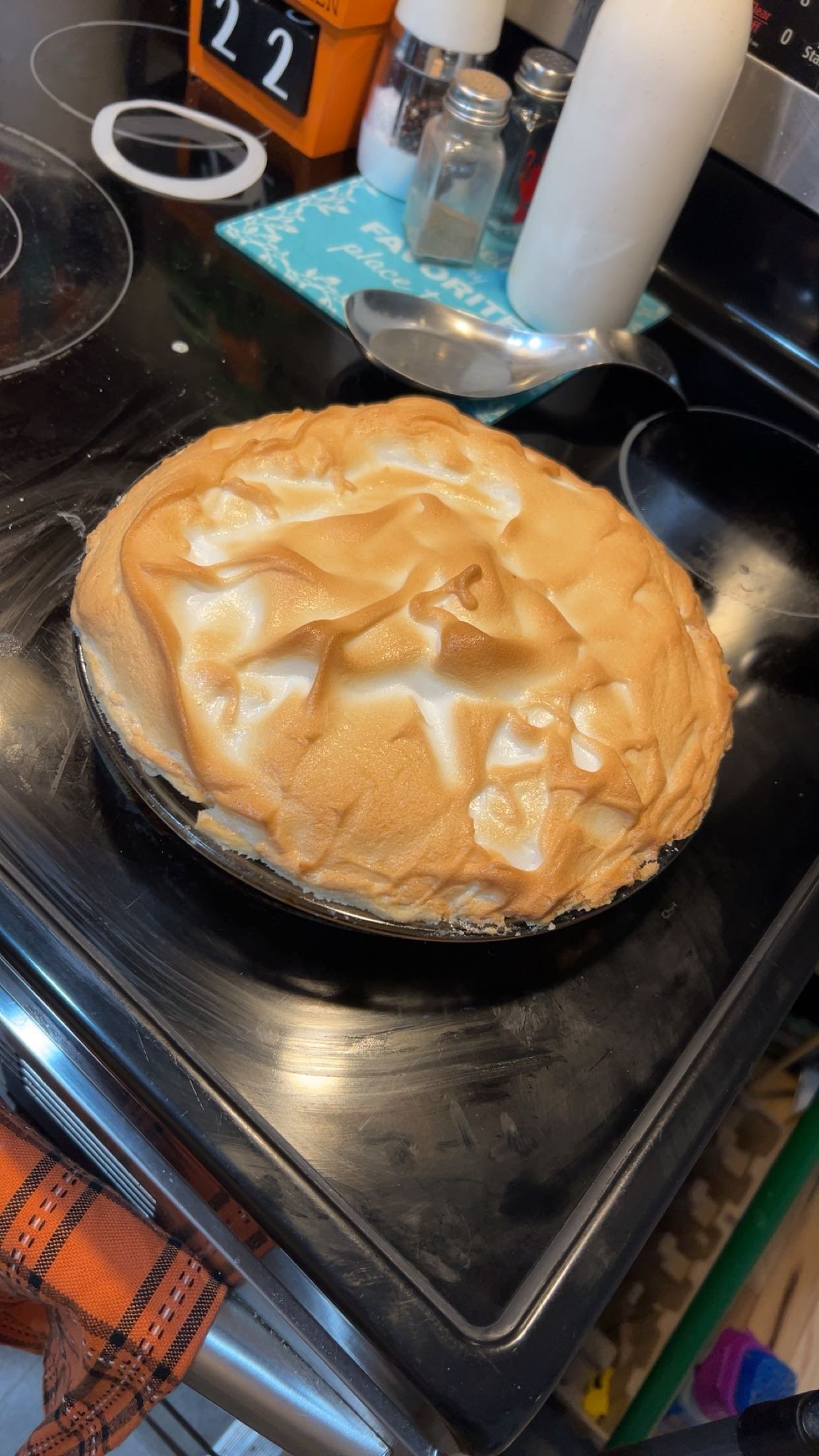 A homemade lemon meringue pie with a toasted meringue topping on a black stovetop in a kitchen setting.
