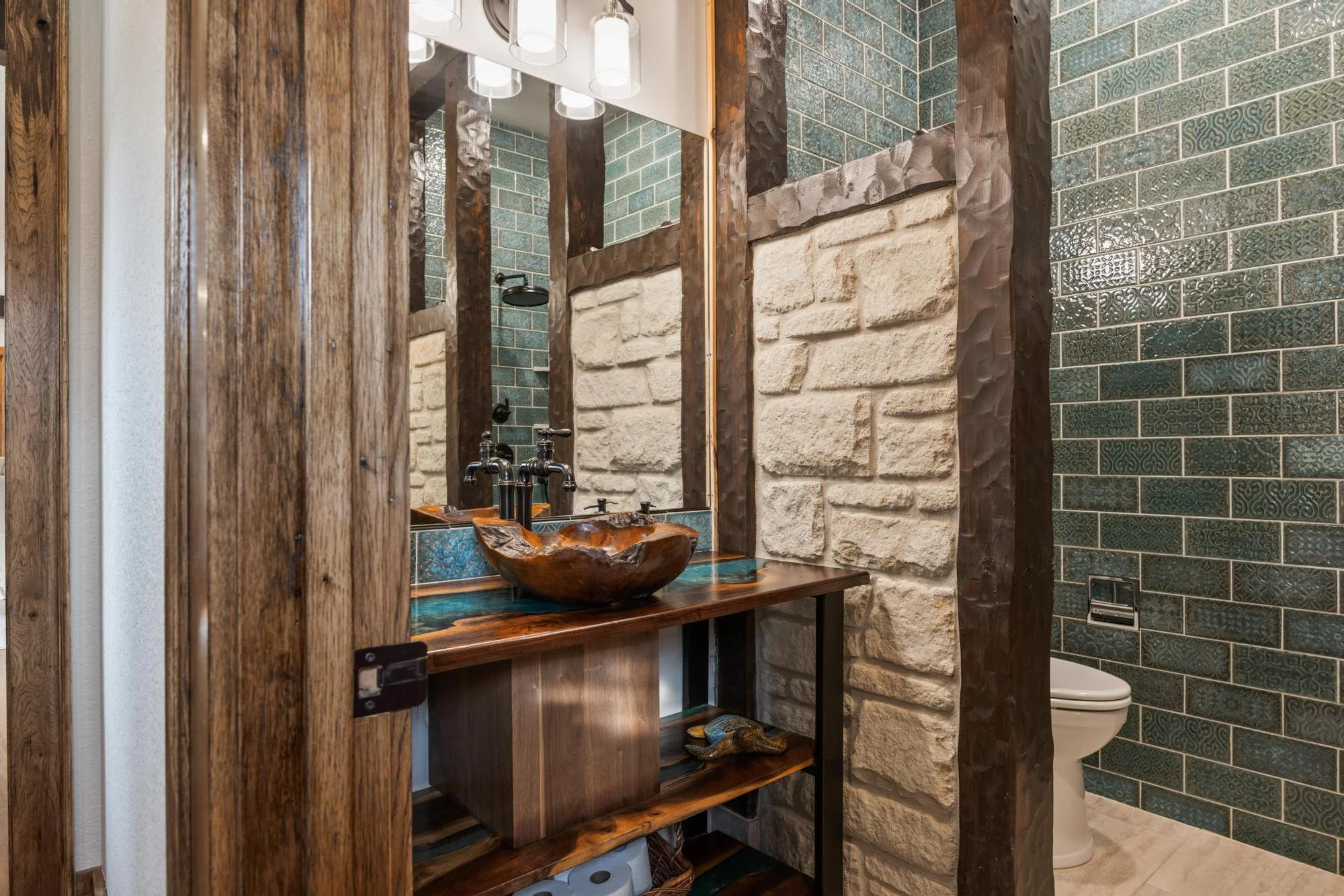 Rustic bathroom with wood and stone accents, featuring a wooden vanity with a unique wooden sink, a large mirror, textured brown wood framing, and vintage-style accents on the walls.
