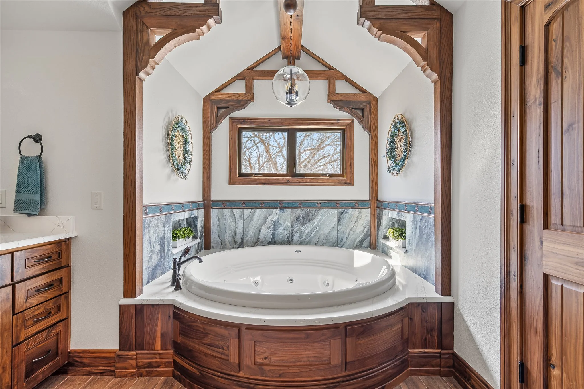 Bathroom with a corner bathtub surrounded by wooden framing, a window with a view of trees, and wood accents on the ceiling and walls.