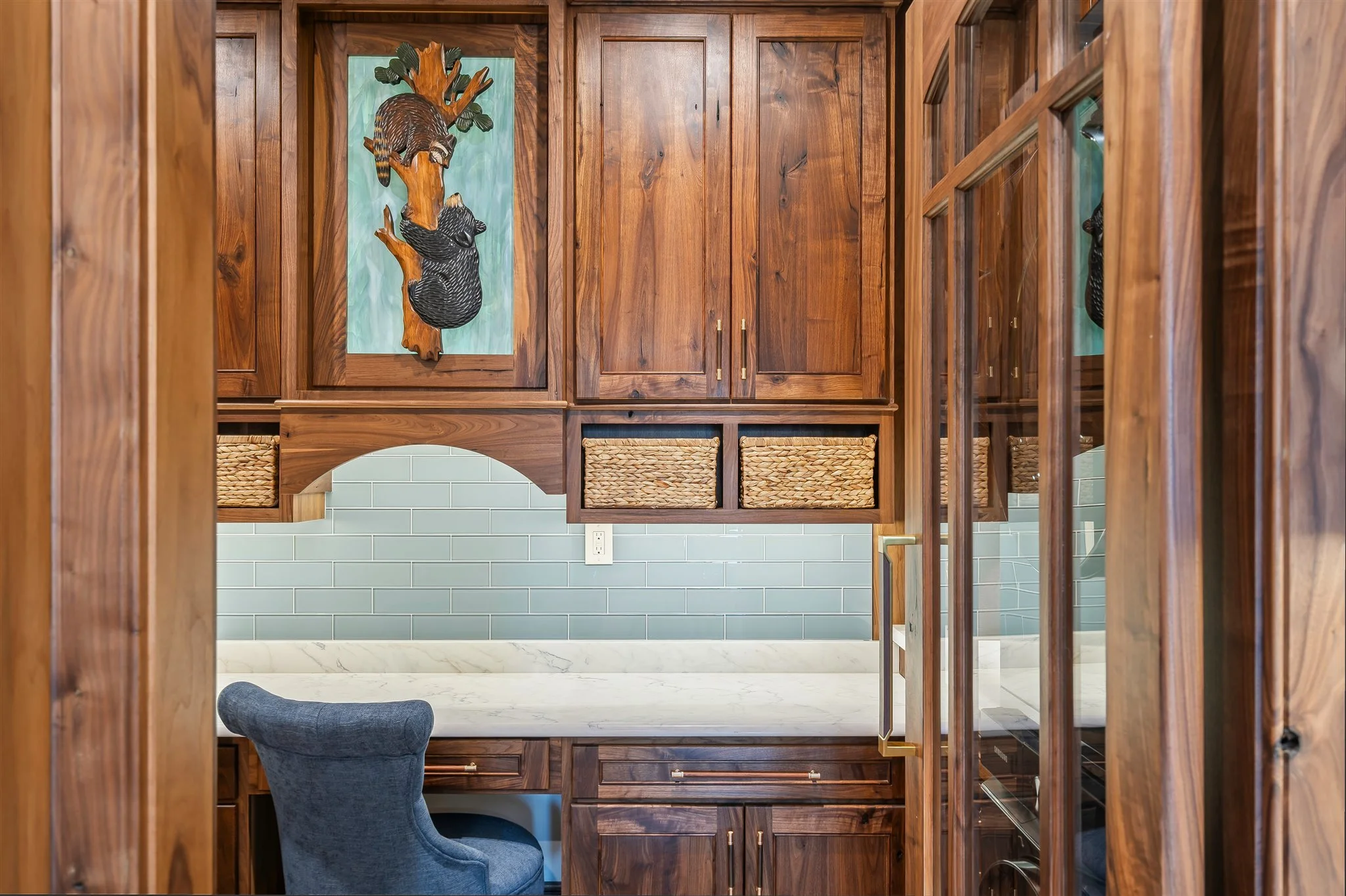 View of a kitchen with wooden cabinetry, light green subway tile backsplash, and a marble countertop. A blue upholstered chair is partially visible at the bottom.
