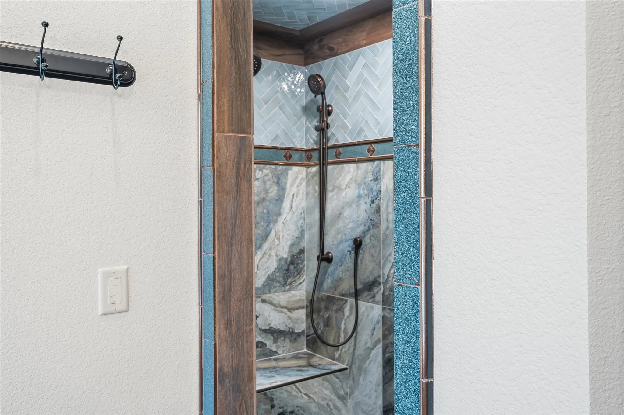 View of a shower area through a mirror, featuring a hand-held showerhead, mosaic wall tiles, and wood accents.