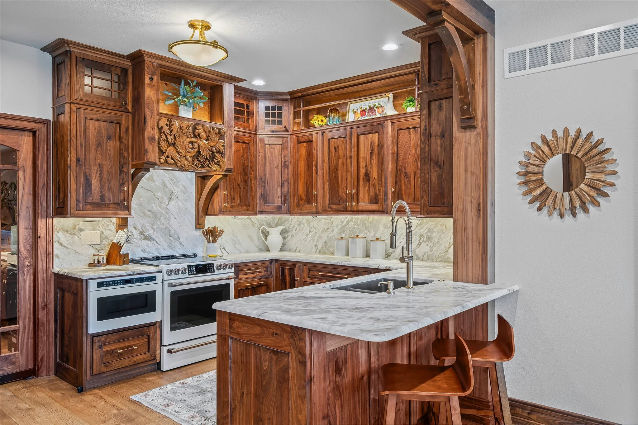 Kitchen with wooden cabinetry, marble countertops, and white appliances, including stove and oven, with decorative items on open shelves and a round mirror on the wall.