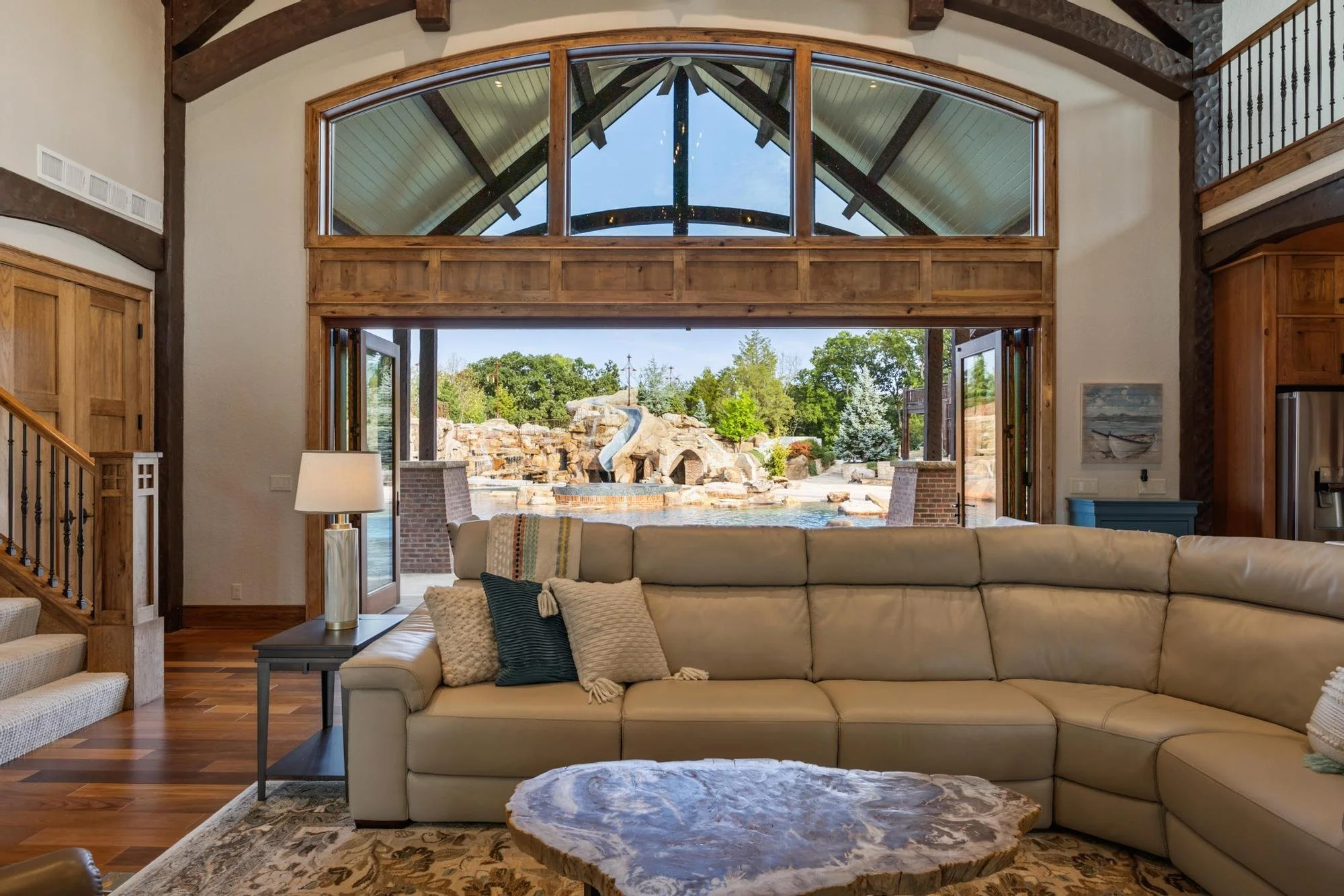 Living room with large arched window and view of backyard with water feature, trees, and rock formation.