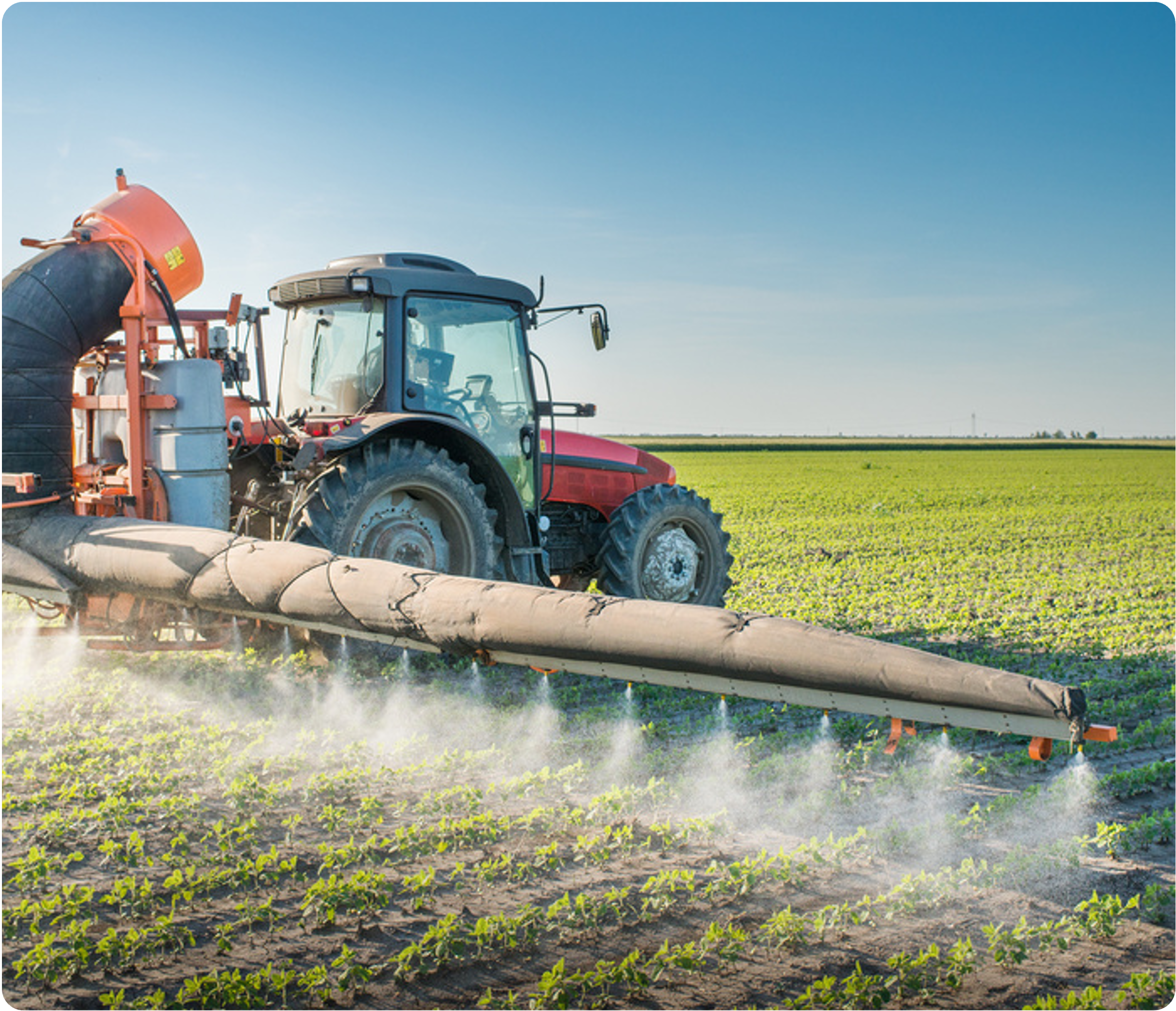 A red tractor with a large spraying apparatus operating in a green field under a clear blue sky.
