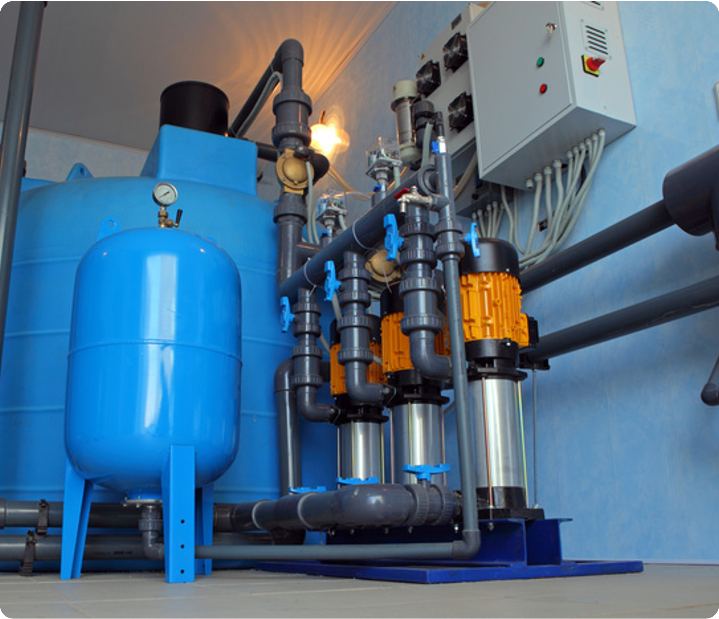 Water filtration system with blue tanks, pipes, and control panel against a light blue wall.