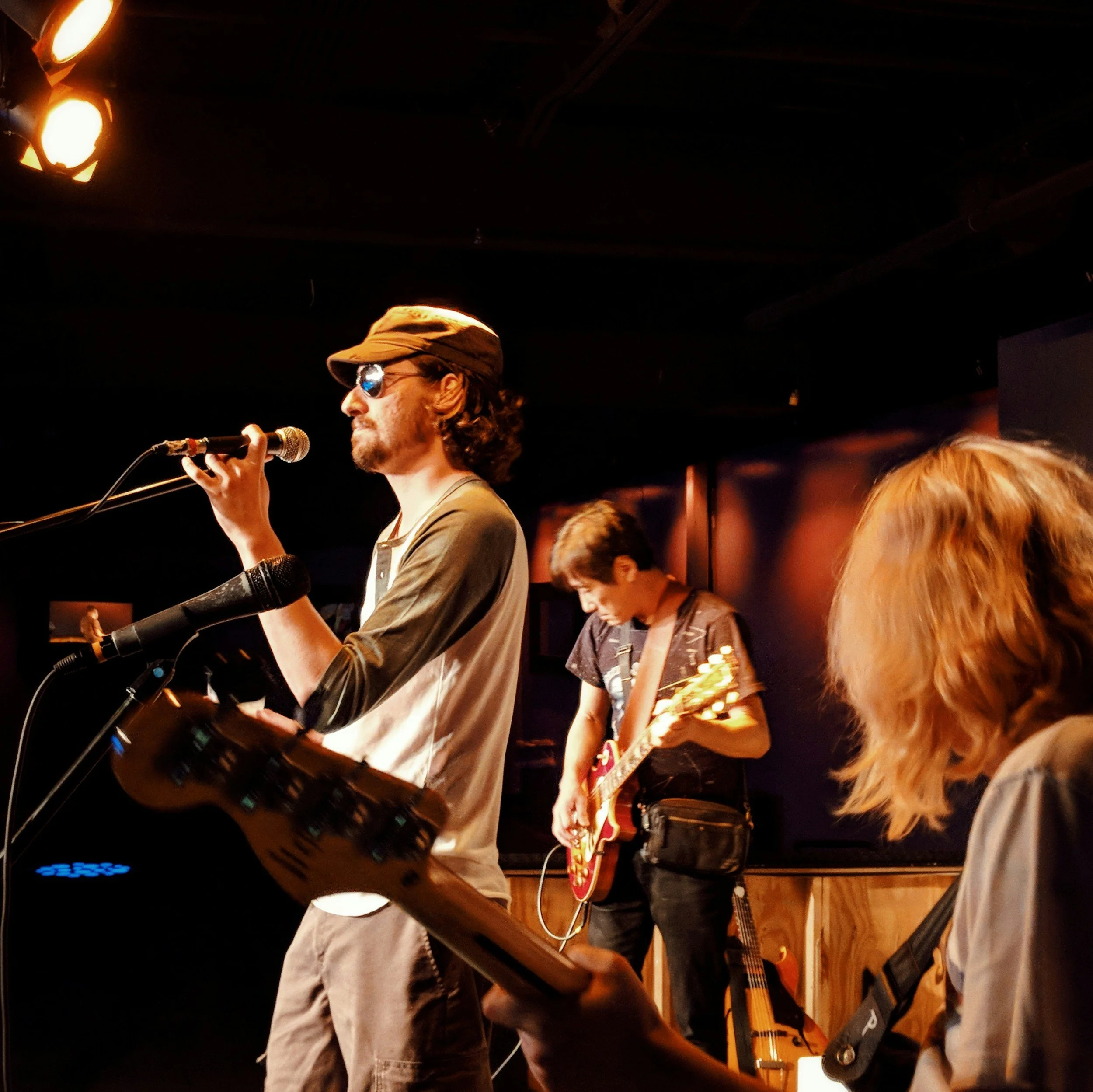 A musician is singing into a microphone while another person plays guitar during a live performance on stage with dim lighting.